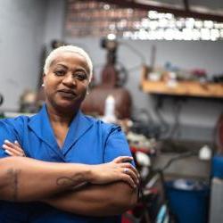 一名黑人妇女，穿着蓝色衬衫，双手交叉在机械店 