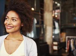 Female black business owner smiling in front of open business doors.